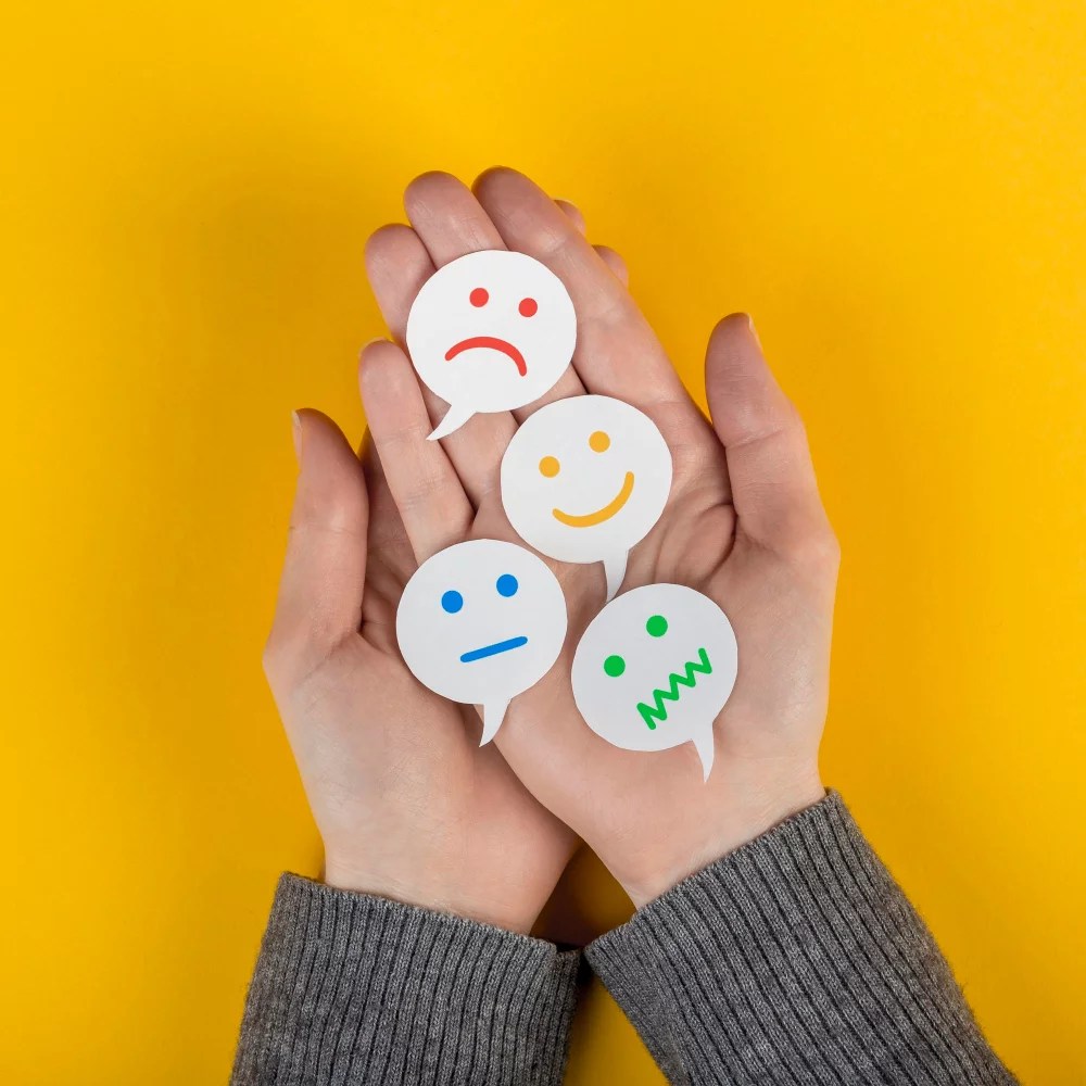 Hands holding paper faces with emotions drawn on them.